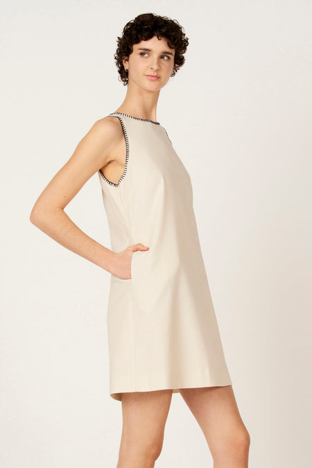 Mouwtjesloze ecru kleedje van Le Fabuleux Marcel de Bruxelles, met zwarte stiksels rond de halslijn en armsgaten.