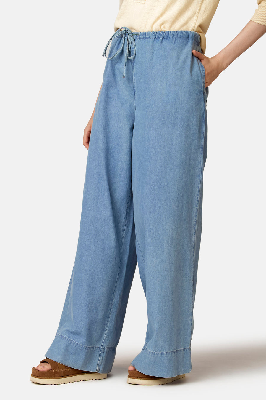 Jean en denim bleu clair coupe large de Le Fabuleux Marcel de Bruxelles, avec une taille haute et des sandales marron.