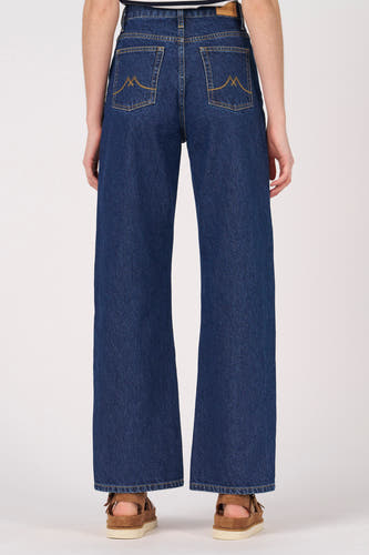 Donkerblauwe wijde jeans van Le Fabuleux Marcel de Bruxelles, met opgestikte zakken aan de achterkant, gedragen met bruine sandalen.
