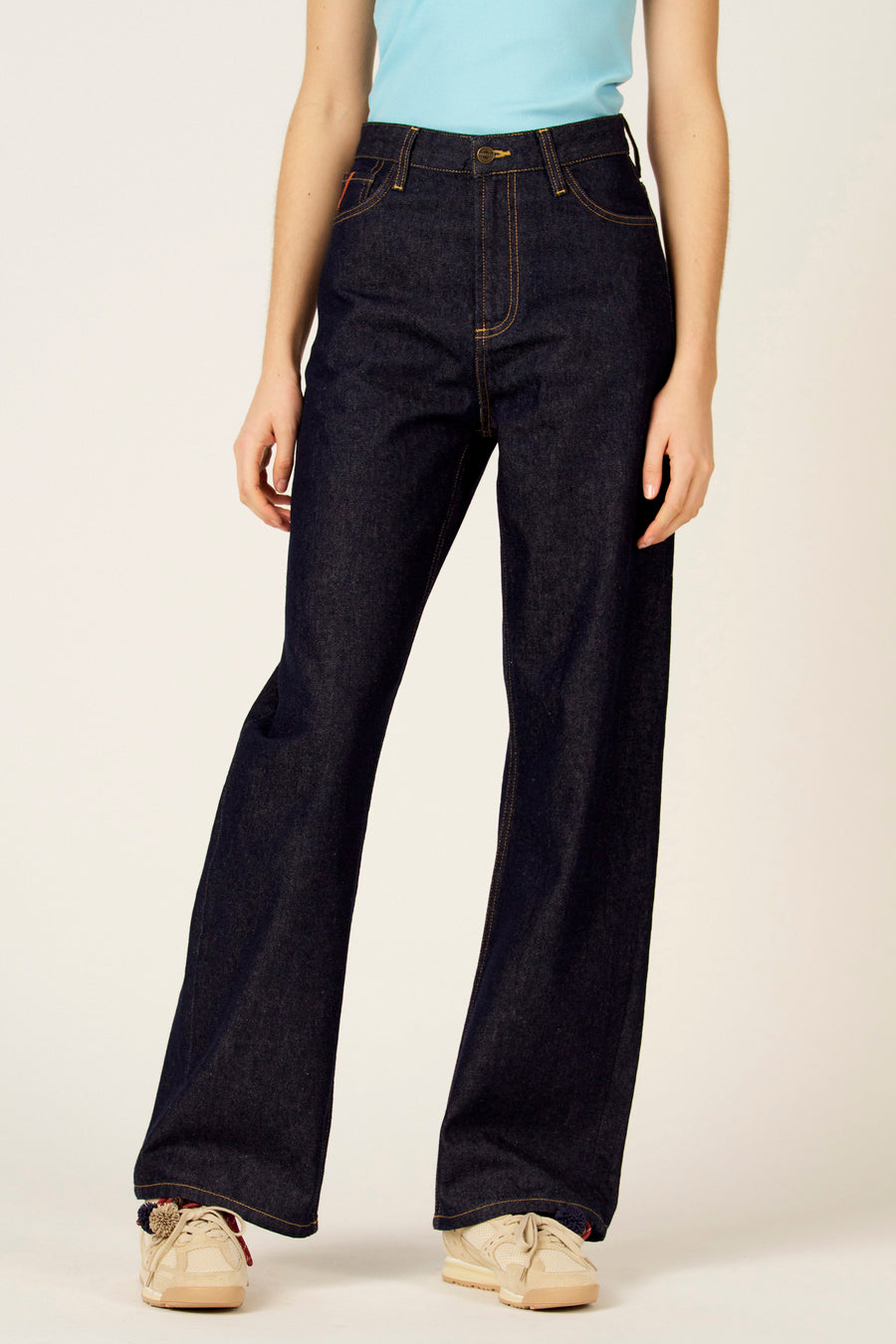 Wijde denim jeans van Le Fabuleux Marcel de Bruxelles, met oranje stiksels en beige sneakers.

