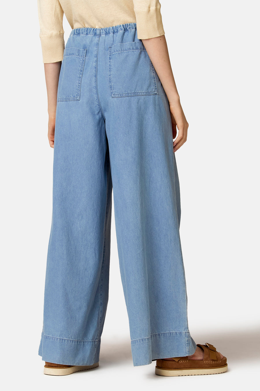 Jeans larges en denim bleu clair de Le Fabuleux Marcel de Bruxelles, avec taille élastique et poches arrière, combinées avec des sandales marron.
