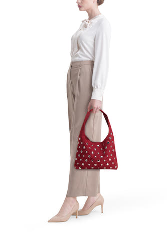 Rode schoudertas van My Jewellery Bags, gedecoreerd met zilverkleurige studs, gedragen met een witte blouse en beige pantalon.
