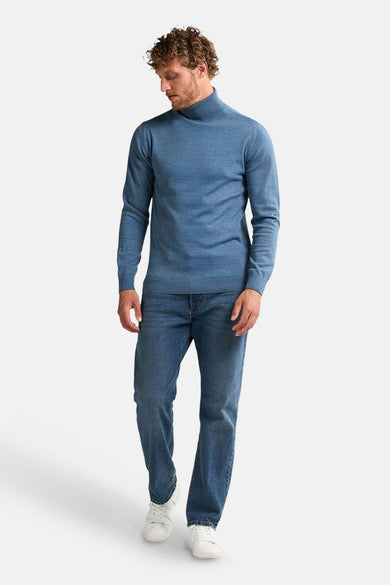 Blauwe trui met rolkraag van Petrol Industries, gedragen met jeans en witte sneakers.
