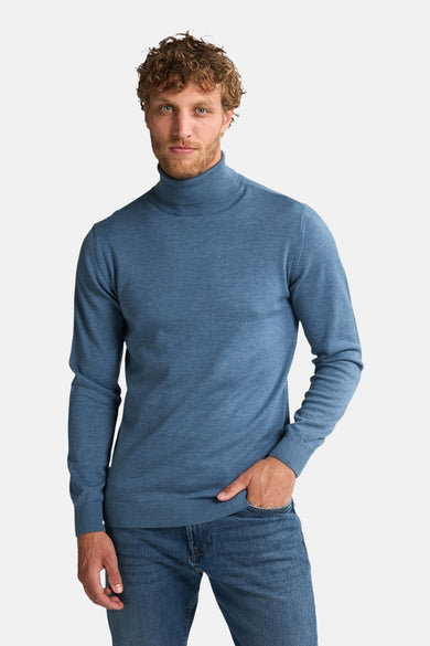 Blauwe coltrui van Petrol Industries, gedragen met jeans en één hand in de broekzak.