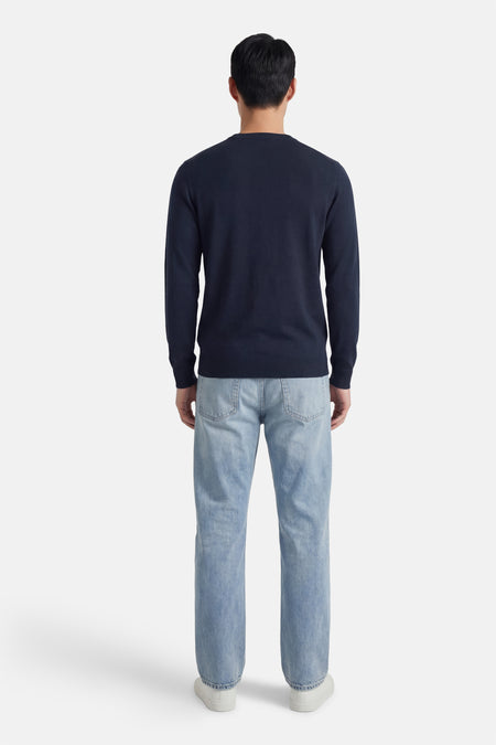 Pull bleu à col rond de Petrol Industries®, vu de dos avec un jean clair et des chaussures blanches.
