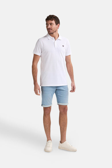 Witte polo met korte mouwen van Petrol Industries, gedragen met denim shorts en witte sneakers.
