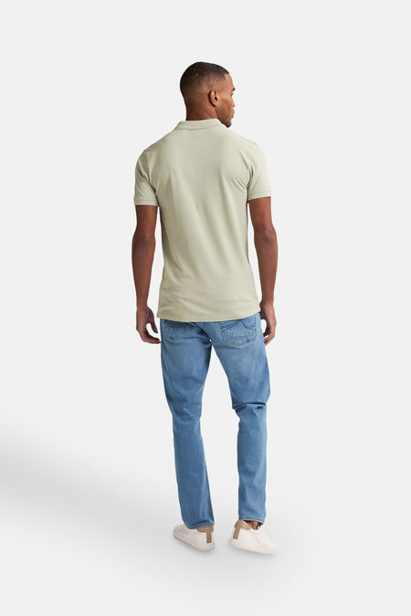 Groene polo met korte mouwen van Petrol Industries, gezien van achteren, met blauwe jeans en witte sneakers.
