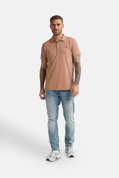 Polo marron à manches courtes de Petrol Industries, porté avec des jeans et des baskets blanches.
