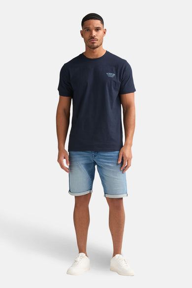 Blauwe jeansshort van Petrol Industries, gecombineerd met een donkerblauw T-shirt en witte sneakers.