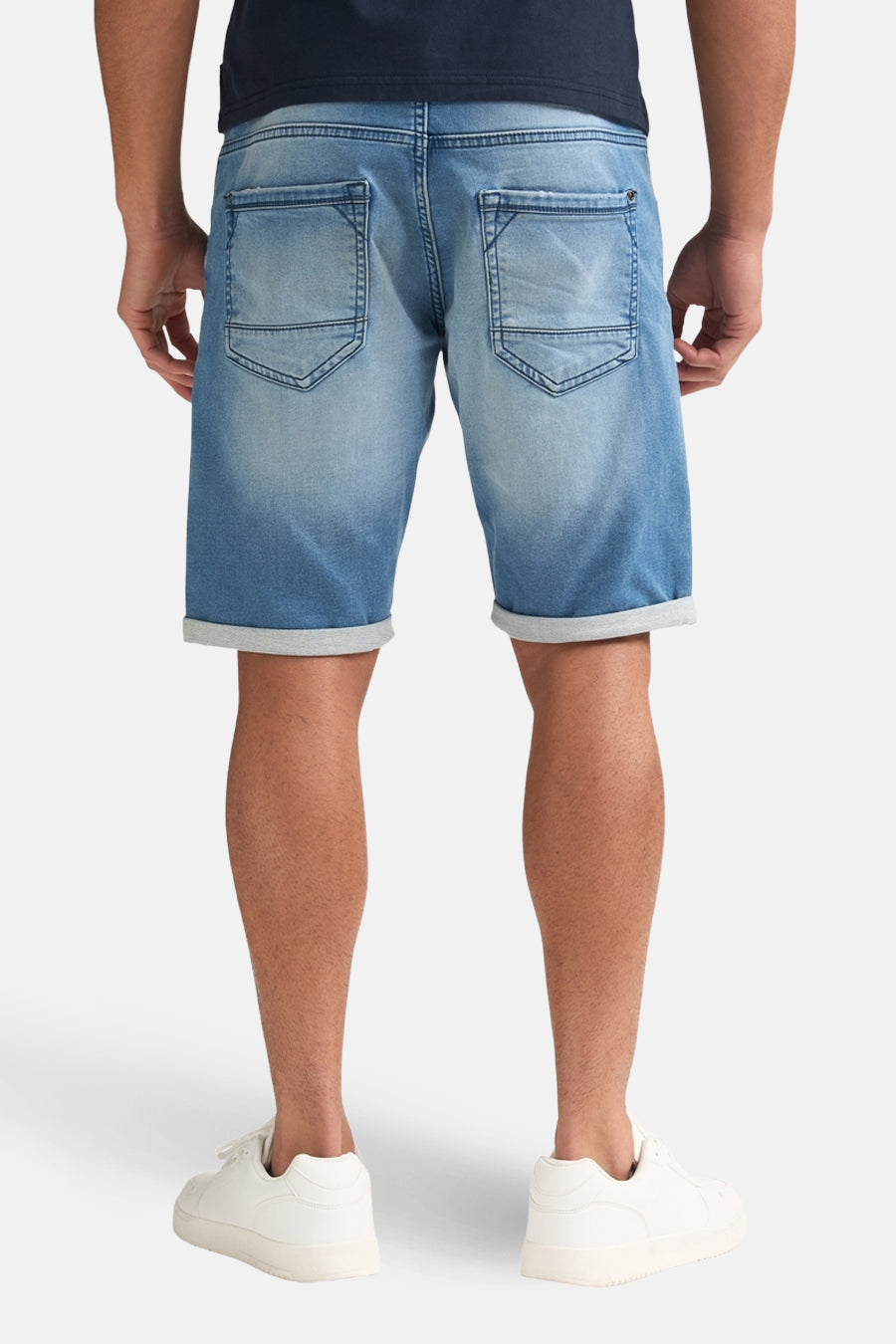 Blauwe jeansshort van Petrol Industries, gezien van achteren, met opgerolde pijpen en witte sneakers.
