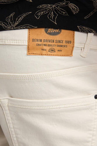 Ecru denim short van Petrol Industries®, met bruin leren merklabel en een zwart shirt met bladpatroon.