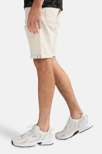 Ecru short van Petrol Industries met omgeslagen pijpen, gedragen door een man met witte sneakers.