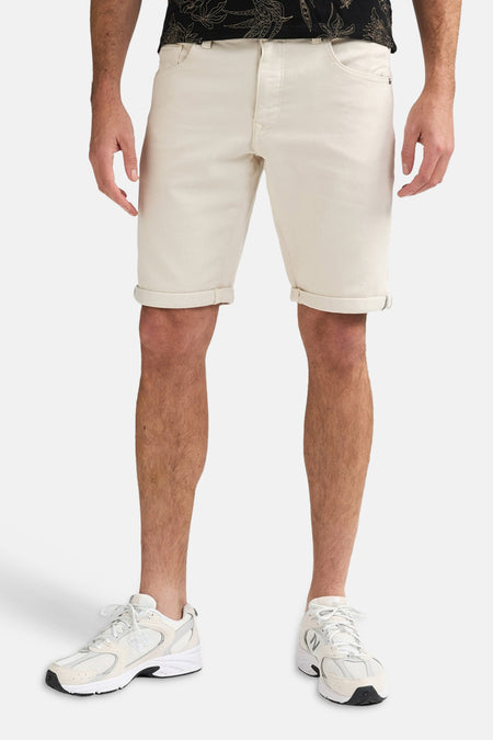 Ecru short van Petrol Industries met omgeslagen zomen, gedragen door een man met een donker shirt en witte sneakers.