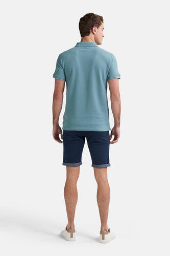 Donkerblauwe short van Petrol Industries met opgerolde pijpen, gecombineerd met een lichtblauw poloshirt en witte schoenen, gezien van achteren.