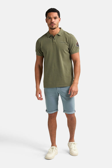 Blauwe short van Petrol Industries, met opgerolde pijpen, gecombineerd met een olijfgroene polo en crèmekleurige sneakers.