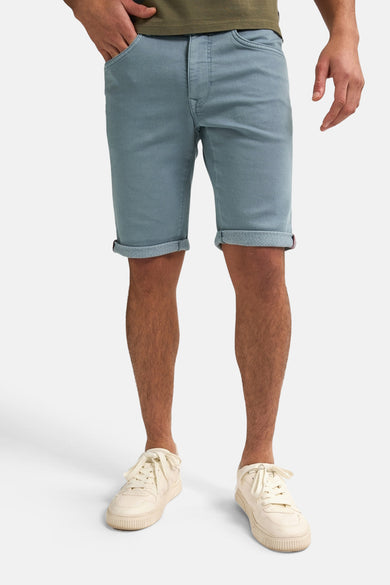 Blauwe short van Petrol Industries, met opgerolde pijpen en gedragen met crèmekleurige sneakers en een olijfgroen shirt.
