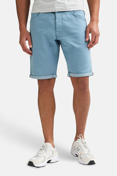 Blauwe short van Petrol Industries® met opgerolde zomen, gedragen door een man met een grijs gestreept T-shirt en witte sneakers.