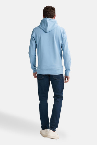 Blauwe sweater met kap van Petrol Industries, gezien van achteren, gecombineerd met donkerblauwe jeans en ecrukleurige schoenen.