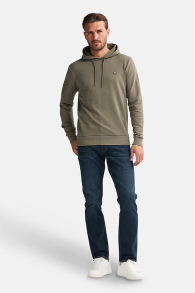 Groene sweater met kap van Petrol Industries®, met trekkoorden en effen donkerblauwe jeans en witte sneakers.
