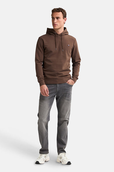 Pull-over marron avec capuche de Petrol Industries, porté avec des jeans gris et des baskets blanches.