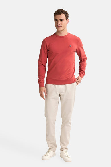 Rode sweater van Petrol Industries, met lange mouwen en subtiel logo op de borst, gecombineerd met een beige broek en schoenen.
