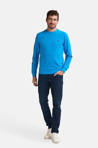 Pull-over bleu de Petrol Industries, avec des manches longues, associé à des jeans noirs et des baskets blanches.