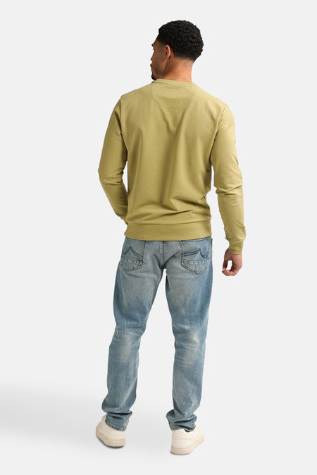 Groene sweater van Petrol Industries, rugzijde gezien, met jeans en crèmekleurige sneakers.

