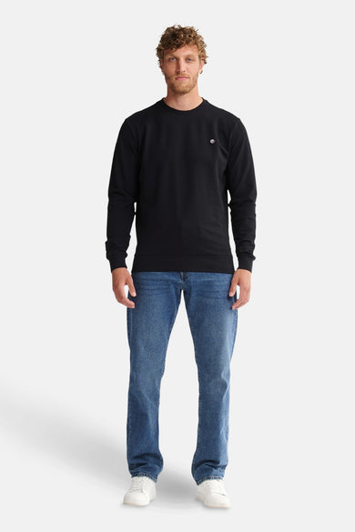Zwarte sweater van Petrol Industries, met lange mouwen, gedragen met een blauwe jeans en witte sneakers.