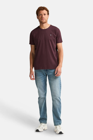 Bordeaux T-shirt met korte mouwen van Petrol Industries, gedragen met jeans en witte sneakers.
