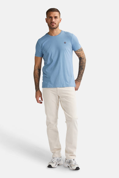 T-shirt bleu à manches courtes de Petrol Industries, porté avec des jeans beige et des baskets.