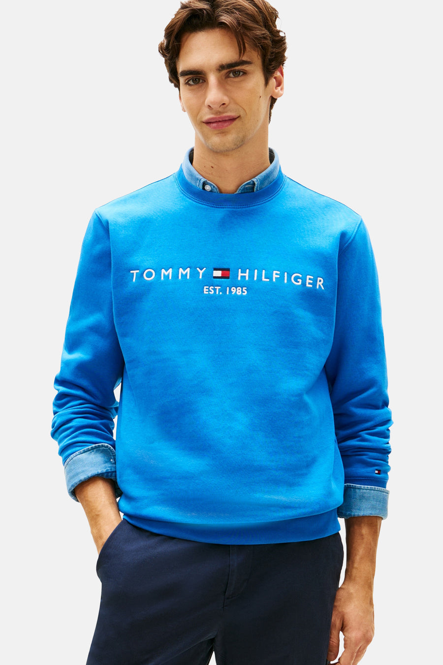 Blauwe sweater met ronde hals van Tommy Hilfiger, gedragen over een denim shirt met marineblauwe broek.