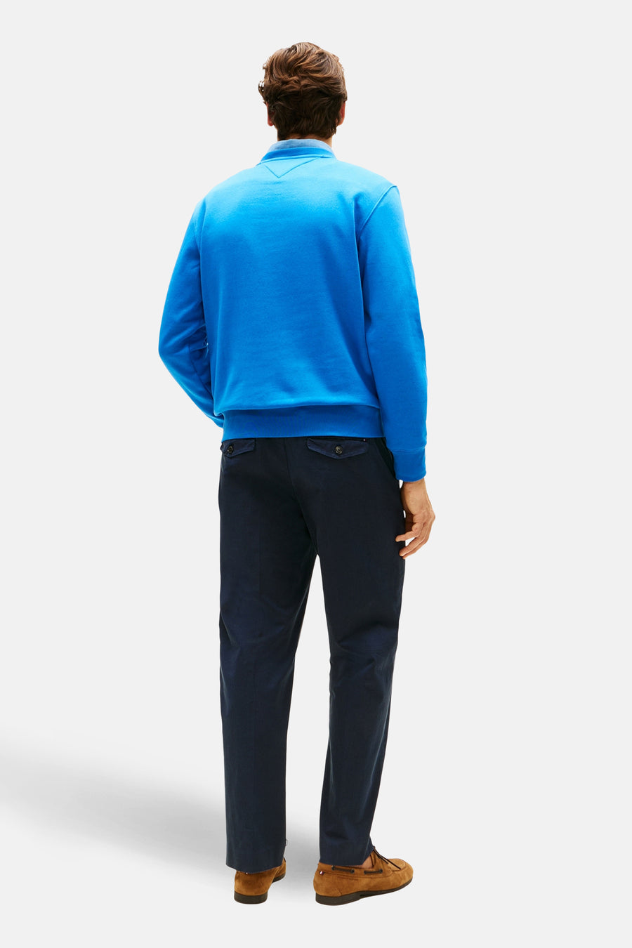 Blauwe sweater met ronde hals van TOMMY HILFIGER, rugzijde, gecombineerd met donkere broek en bruine schoenen.