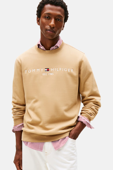 Gilet beige à col rond de TOMMY HILFIGER, porté sur une chemise rayée et associé à un pantalon blanc.