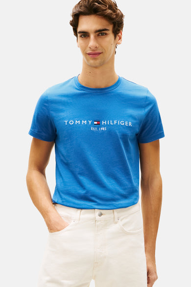 T-shirt bleu à manches courtes de TOMMY HILFIGER, porté avec un short beige et des sandales, dos.