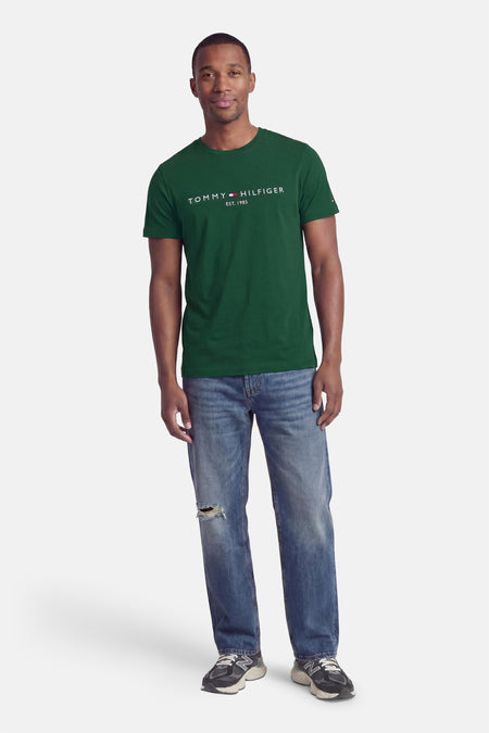 Groene korte mouw T-shirt van TOMMY HILFIGER met wit logo op borst, gedragen met blauwe jeans en sneakers, front view