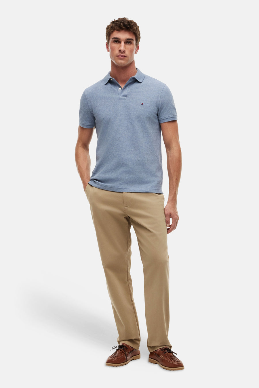 Blauw poloshirt van TOMMY HILFIGER met korte mouwen en knoopjes, gedragen met kaki broek en bruine schoenen.