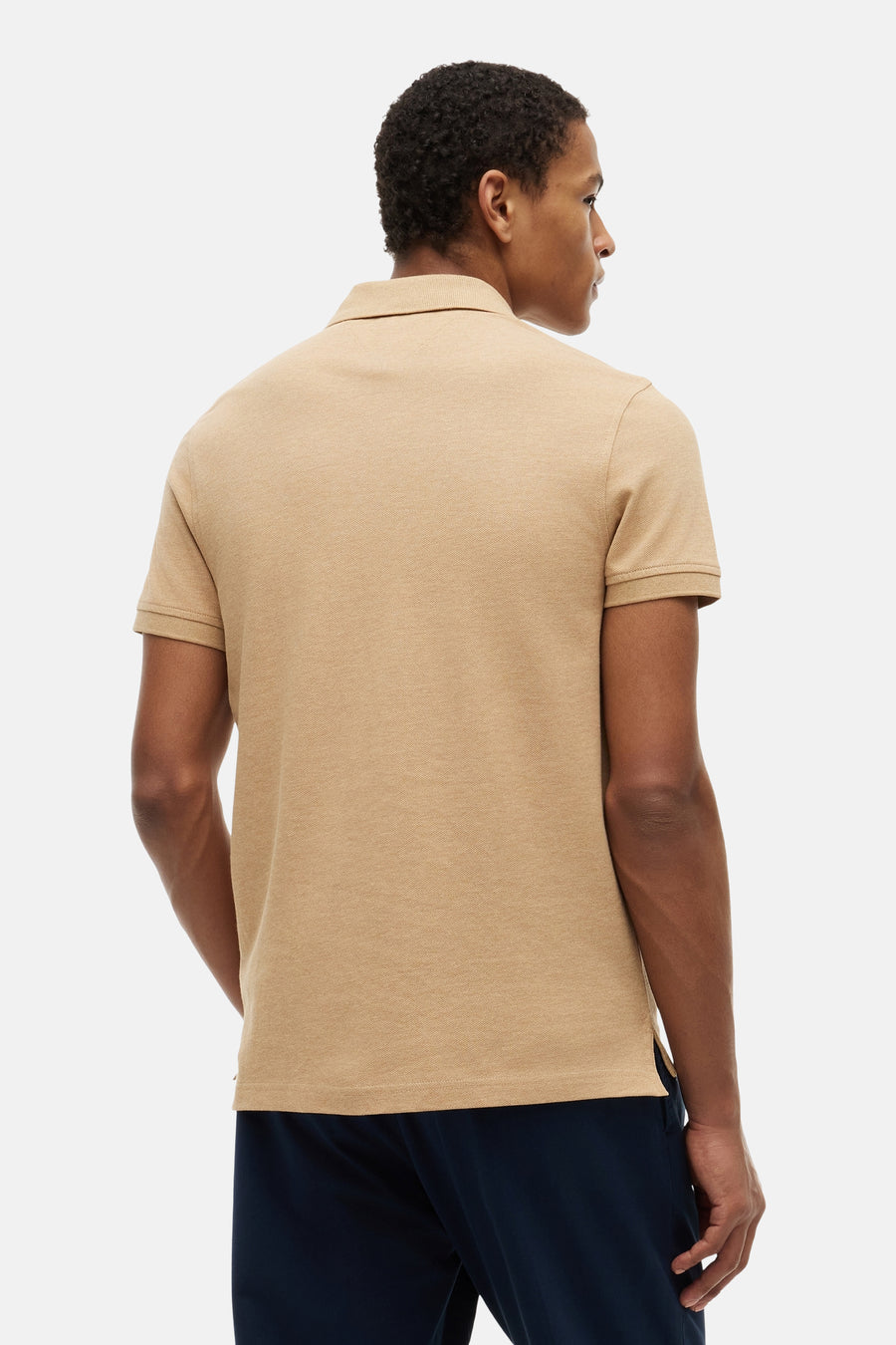 Beige polo van TOMMY HILFIGER, gezien van de achterkant, met een fijne textuur, gedragen door een man met donkerblauwe broek.