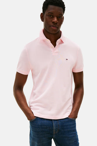 Roze polo met korte mouwen van TOMMY HILFIGER, gedragen met een donkerblauwe jeans met de handen in de zakken.
