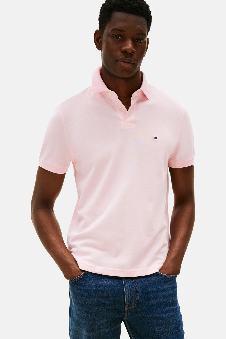 Roze polo met korte mouwen van TOMMY HILFIGER, gedragen met een donkerblauwe jeans met de handen in de zakken.
