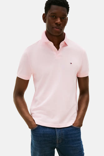 Roze polo met korte mouwen van TOMMY HILFIGER, gedragen met blauwe jeans, met de handen in de zakken.