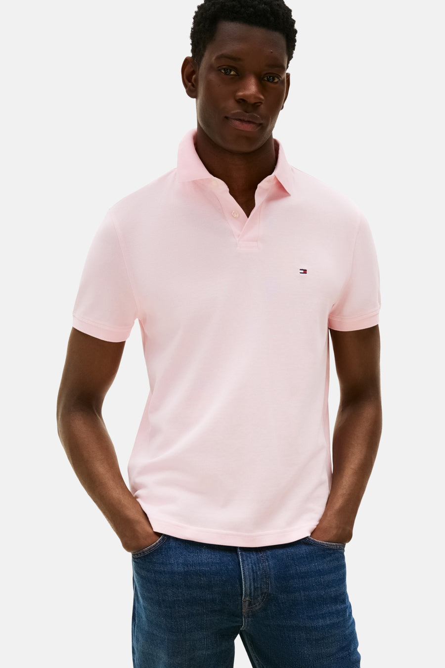 Roze polo met korte mouwen van TOMMY HILFIGER, gedragen met blauwe jeans, met de handen in de zakken.