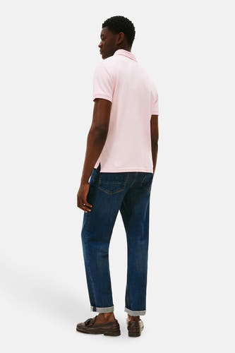 Roze polo met korte mouwen van TOMMY HILFIGER, gezien van achteren, gecombineerd met donkerblauwe jeans en bruine loafers.