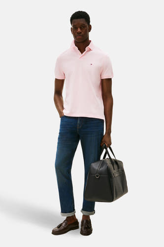 Roze polo met korte mouwen van TOMMY HILFIGER, gedragen met jeans en leren loafers, met een zwarte weekendtas.
