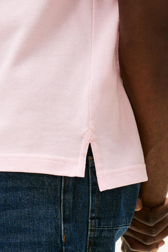 Roze polo met korte mouwen van TOMMY HILFIGER, met een piqué textuur en zijsplit, gedragen met een donkere denim broek.
