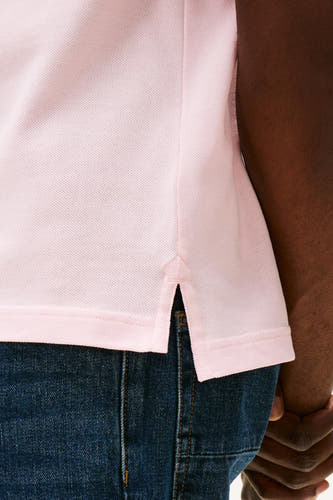 Roze polo van TOMMY HILFIGER, close-up van de onderkant met zijsplitjes en blauwe jeans.
