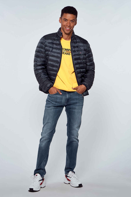 Veste de pluie bleue TOMMY JEANS portée sur un T-shirt jaune et des jeans bleus avec des baskets blanches.