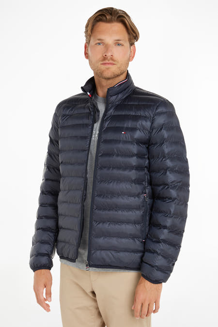 Veste de pluie bleue de TOMMY JEANS, avec des coutures horizontales, sur un modèle portant un t-shirt gris et un pantalon kaki.