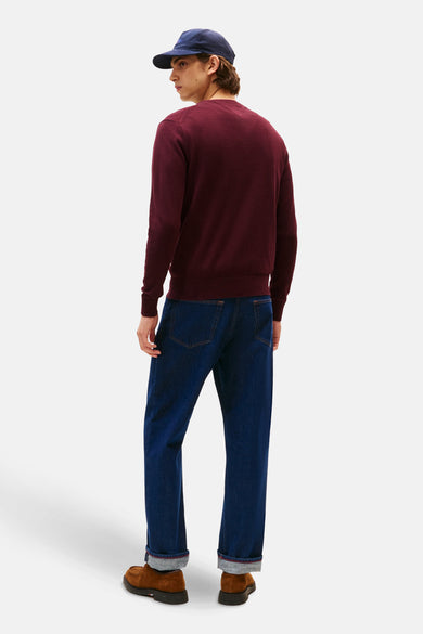Bordeaux trui met ronde hals van TOMMY HILFIGER, gedragen met een donkerblauwe pet, donkere jeans en bruine schoenen, rugaanzicht.
