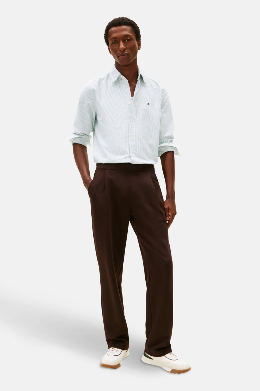 Groen gestreept overhemd met lange mouwen van Tommy Hilfiger, gedragen met bruine pantalon en witte sneakers.
