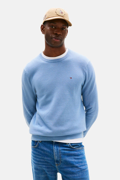 Blauwe trui met ronde hals van Tommy Hilfiger, met klein logo op de borst, gedragen met een jeans en baseballpet.

